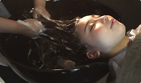 photo:頭髪を洗う女性。瞑目している。
